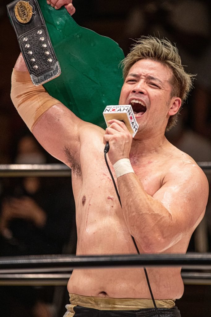 Go Shiozaki on the microphone, with the GHC Heavyweight Championship, in Pro Wrestling NOAH