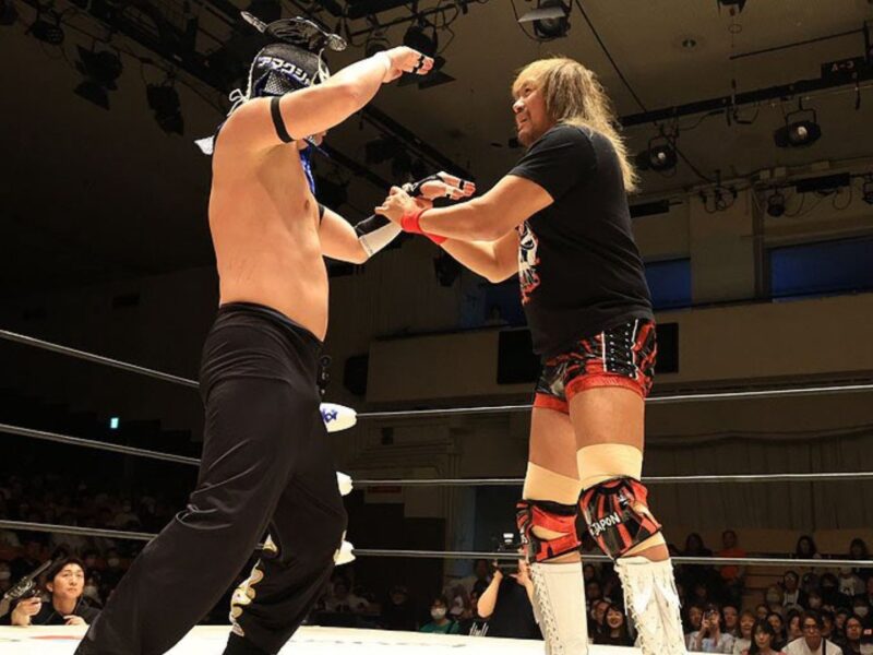 Two wrestlers in a ring lock forearms, facing off as a crowd watches the match.