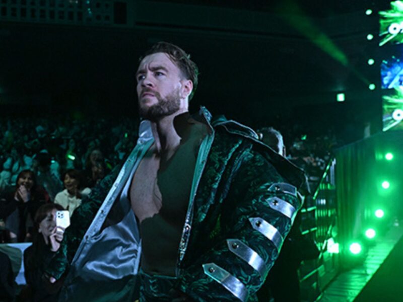 Male wrestler entering a dark arena with green stage lights and cheering crowd in the background.