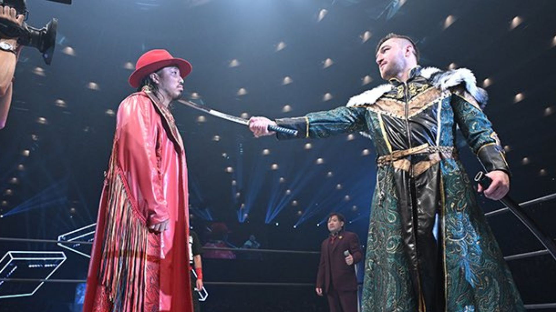 Two performers in ornate costumes stage a duel: one in a red robe and hat, the other in a richly embroidered green cloak, sword pointed between them.