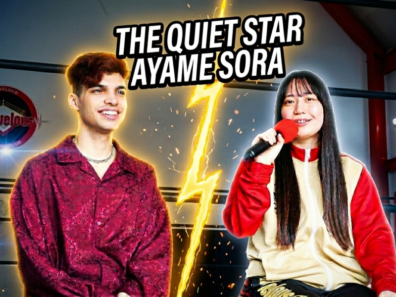 Two young performers in a stage setting; one holds a microphone, with a glowing lightning bolt graphic and bold banner text above them in a ring.