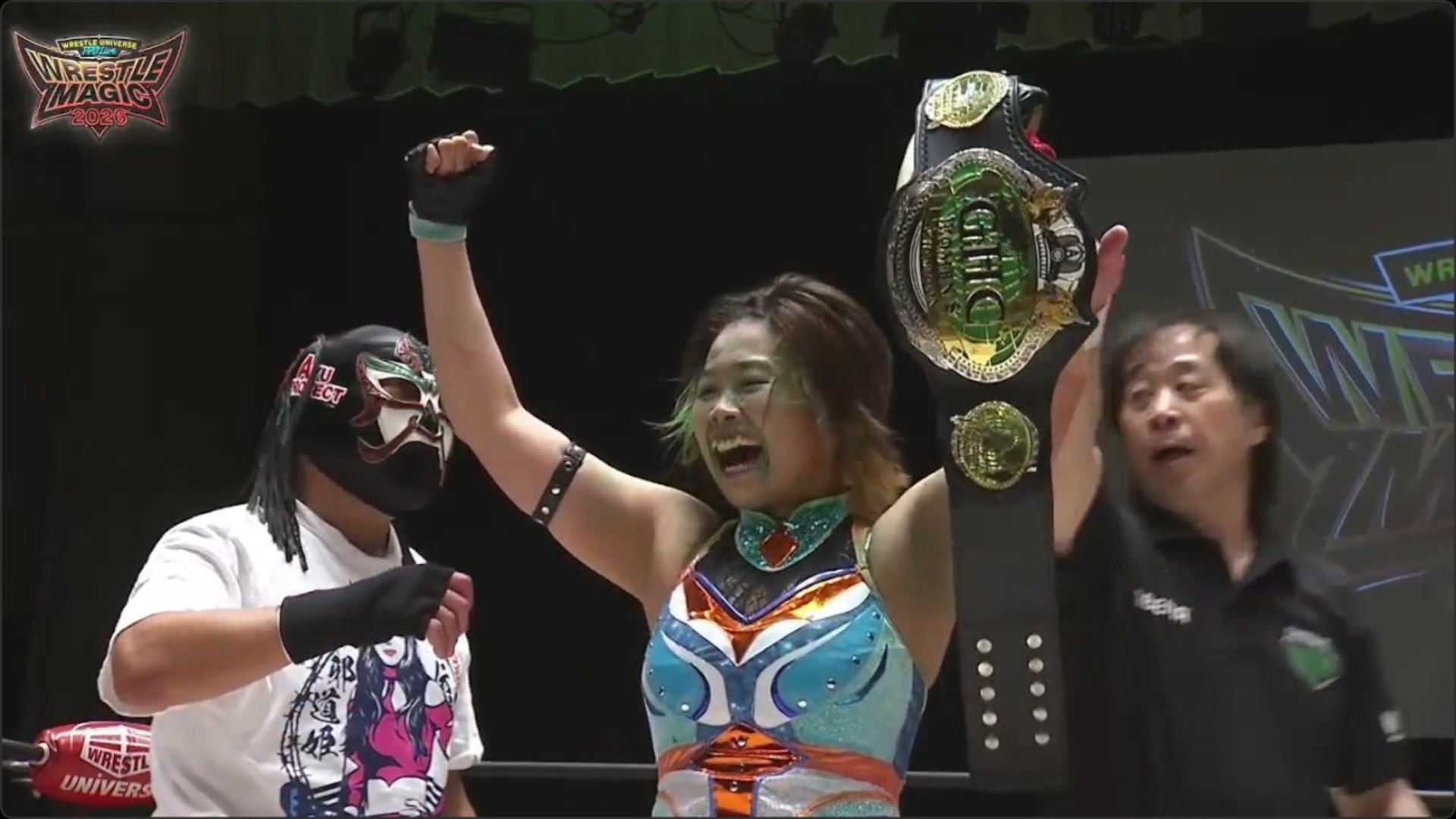Female wrestler celebrates victory, raising a large championship belt above her head on stage.