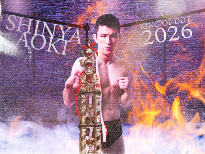 Shirtless young man posing with a tall ornate trophy amid flames and smoke, background text reads 'Shiny Aoki' and 'King of DDT 2026'.
