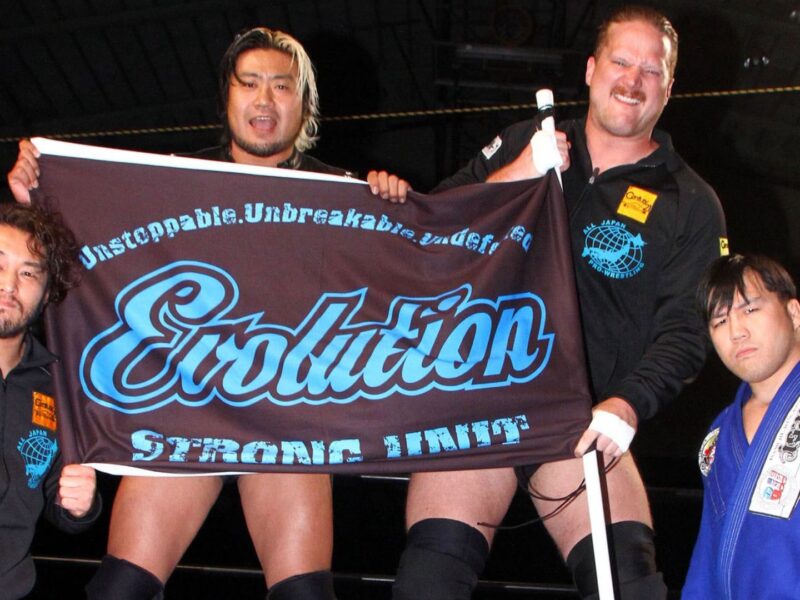 Four wrestlers pose in a ring, holding a large banner that reads Evolution Strong Unit.