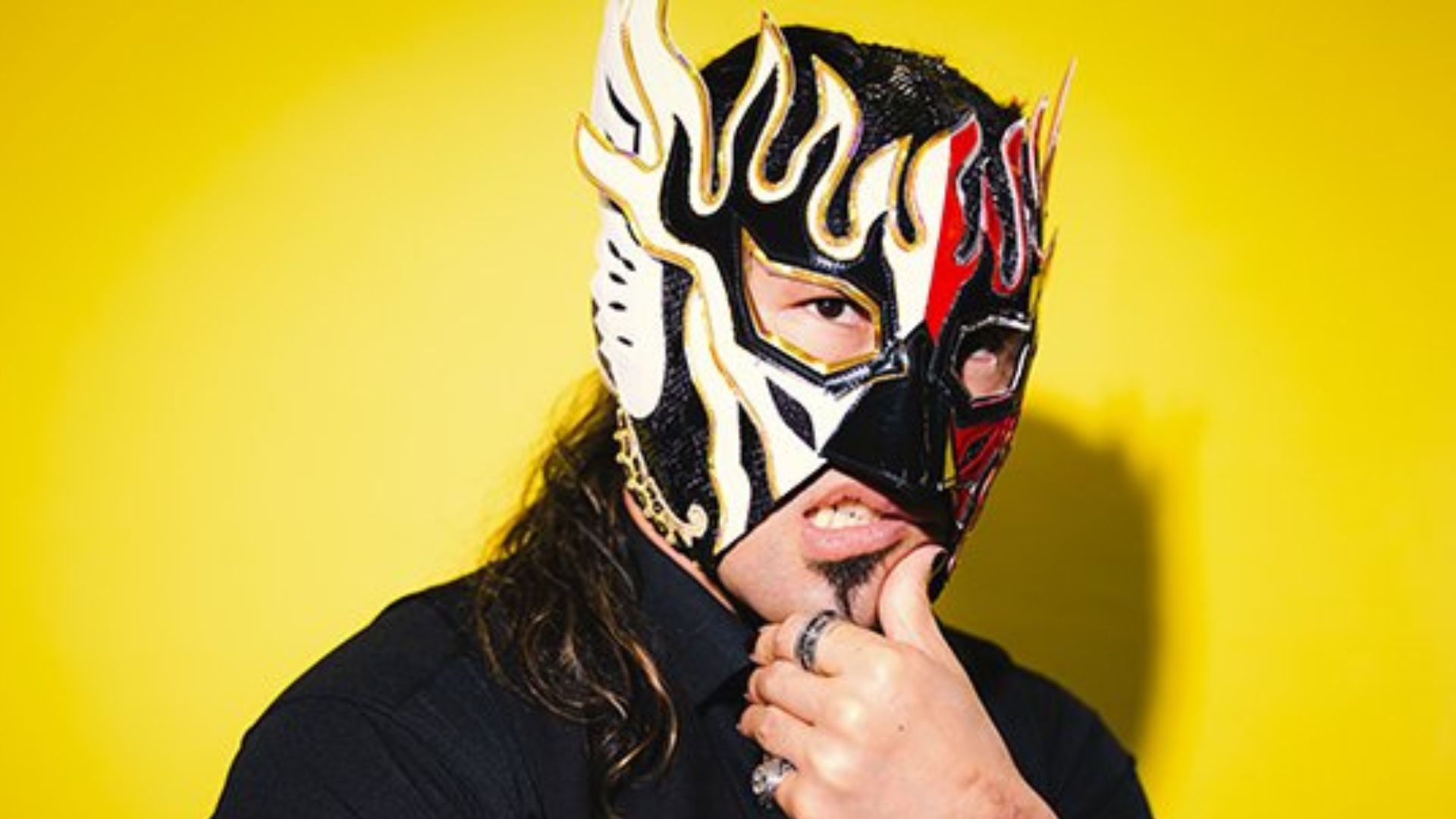 Person wearing a black shirt and a decorative black, white, and red lucha libre mask against a bright yellow background