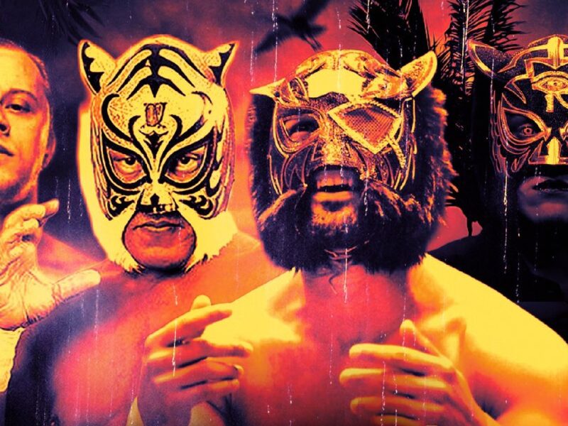 Three masked wrestlers pose with a shirtless man, wearing tiger-themed luchador masks.
