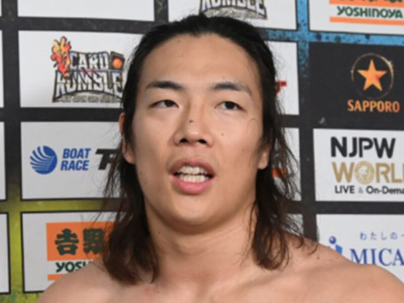 Close-up of an athlete speaking at a post-fight press conference in front of sponsor boards with logos in the background.