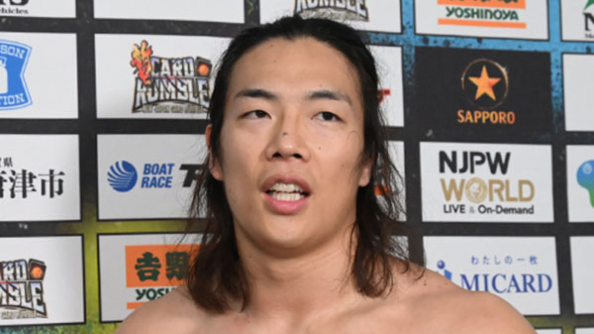 Close-up of an athlete speaking at a post-fight press conference in front of sponsor boards with logos in the background.