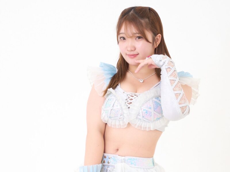 Young woman in pastel cosplay outfit posing with hand near her face against a white background.