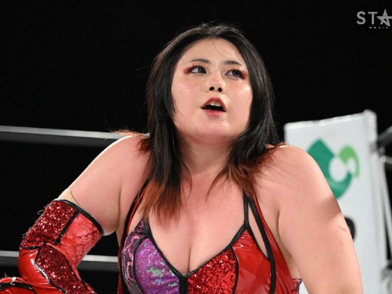 Wrestler in red-sequin attire leans forward inside a ring, looking upward with a focused expression, Stardom logo visible in the corner.