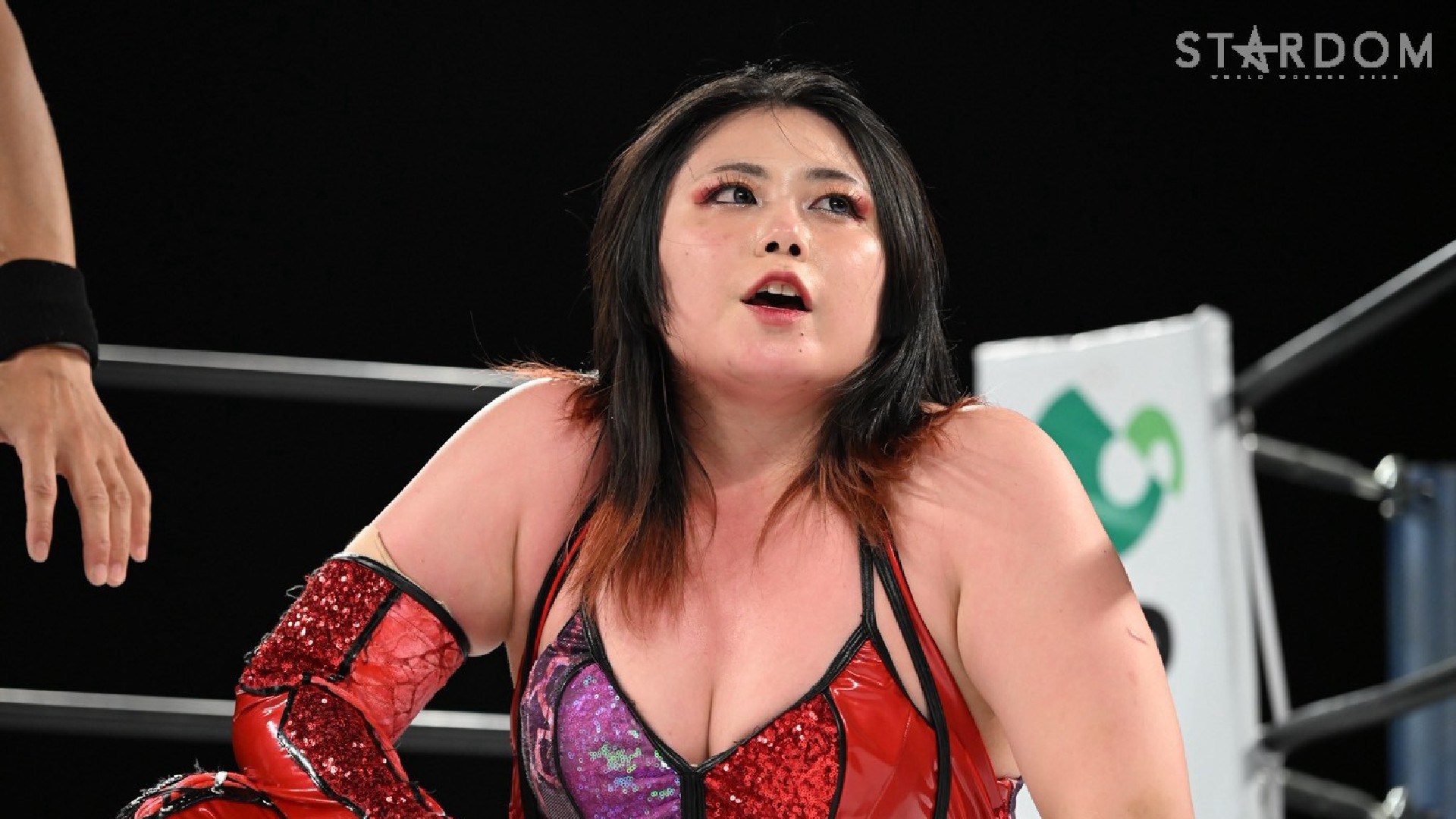 Wrestler in red-sequin attire leans forward inside a ring, looking upward with a focused expression, Stardom logo visible in the corner.