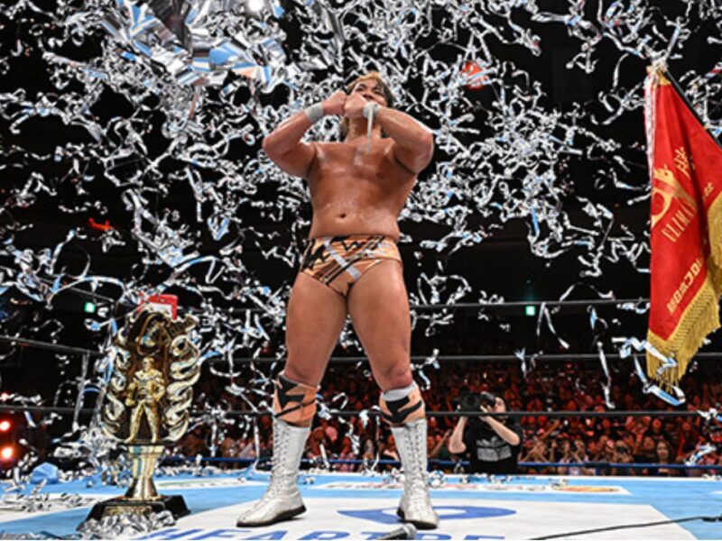 Wrestler in trunks and white boots stands center ring with trophy nearby as silver confetti falls around him.