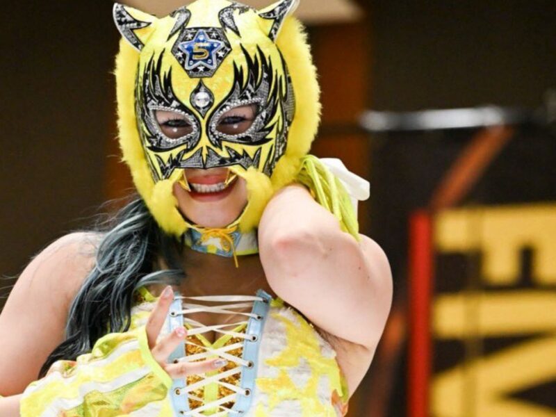 Person in a bright yellow masquerade mask with blue accents, smiling and posing for the camera in a carnival outfit.