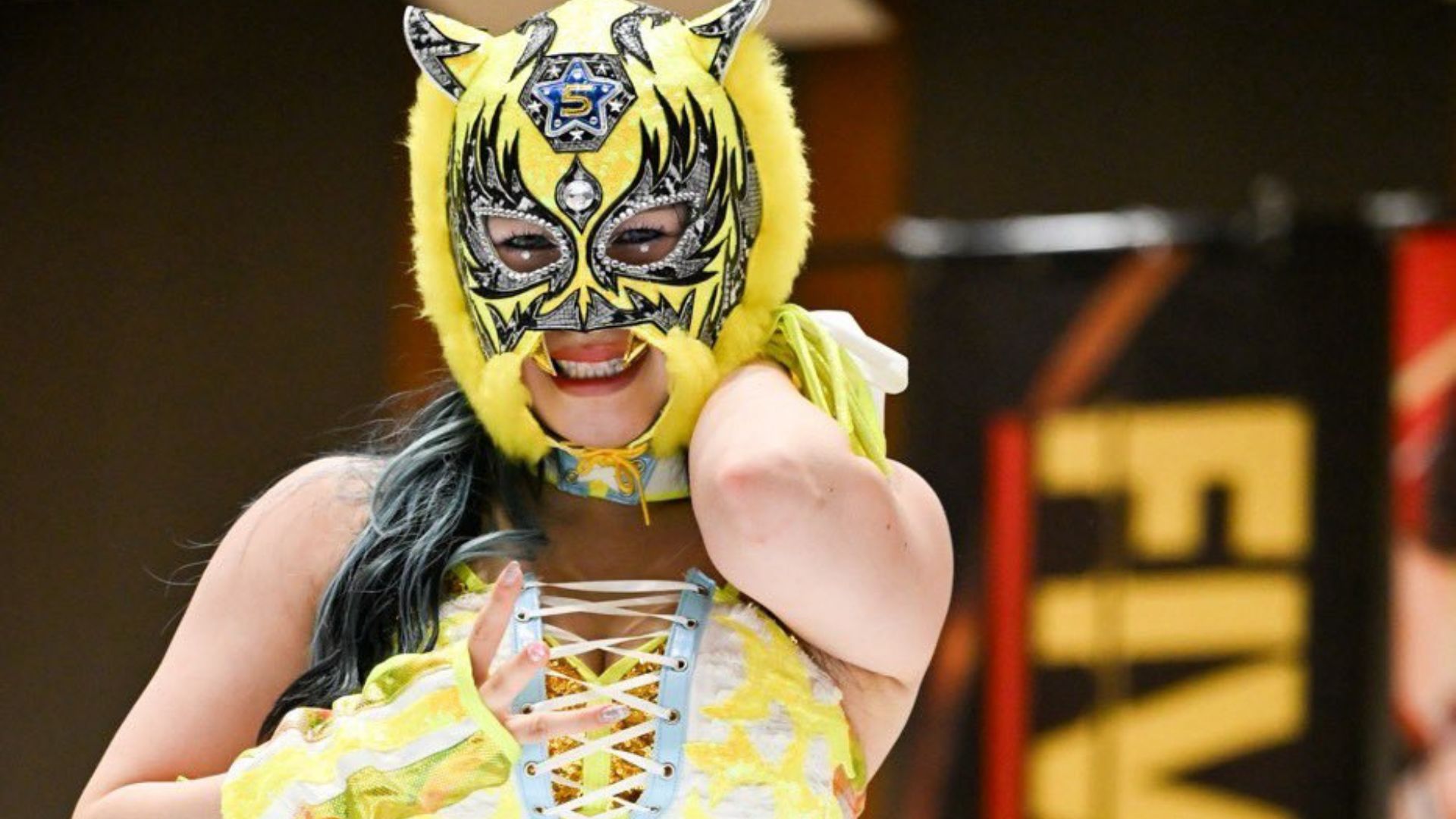 Person in a bright yellow masquerade mask with blue accents, smiling and posing for the camera in a carnival outfit.