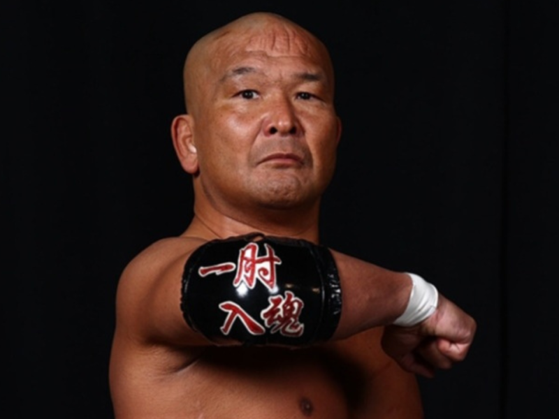 Male martial artist in a fighting pose, his gloved fist extended toward the camera against a dark background. The glove has red Japanese characters on it.