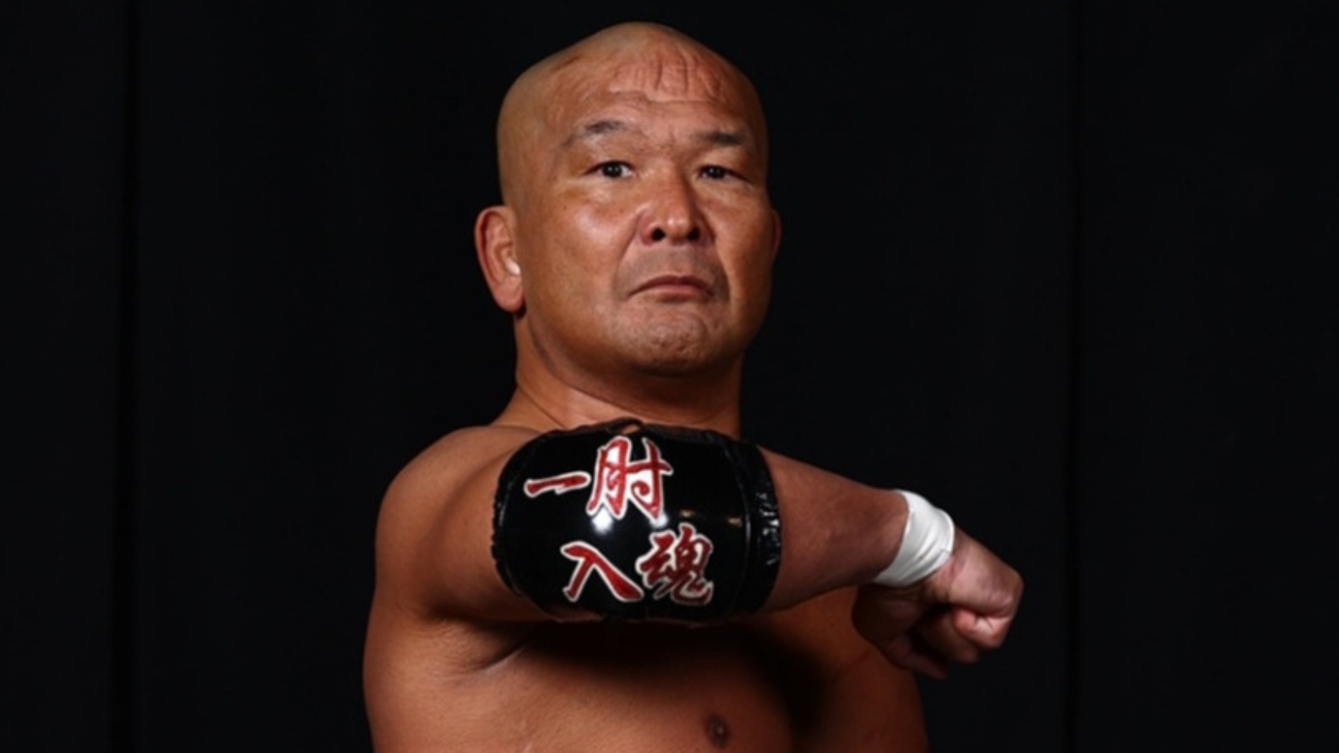 Male martial artist in a fighting pose, his gloved fist extended toward the camera against a dark background. The glove has red Japanese characters on it.